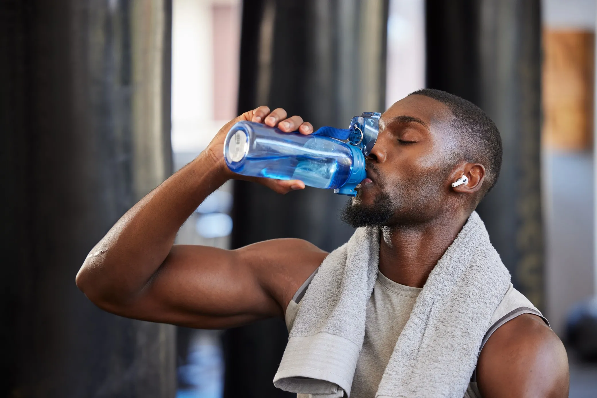 Man drinking from a blue bottle with a towel around his neck.