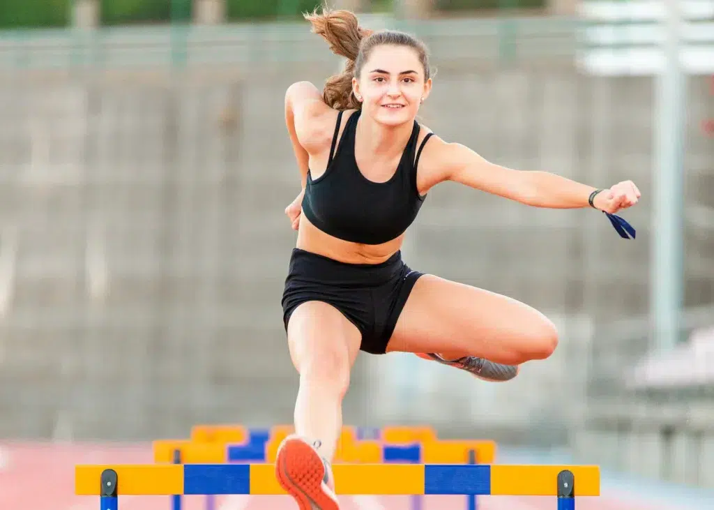young athlete showing resilience jumping over blue and yellow hurdles